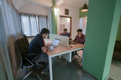 three men sitting at a desk with a laptop computer at Snore Summore, Hostel in Koramangala in Bengaluru