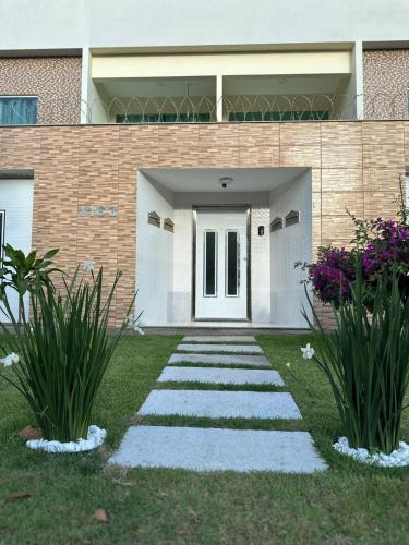 a walkway in front of a house with flowers at Apto Luxo completo 3 quartos em Guriri 300 mts da praia Wi-fi grátis in Guriri
