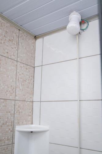 a white tiled bathroom with a toilet and a light at Pousada Tio Bilia in Imbituba