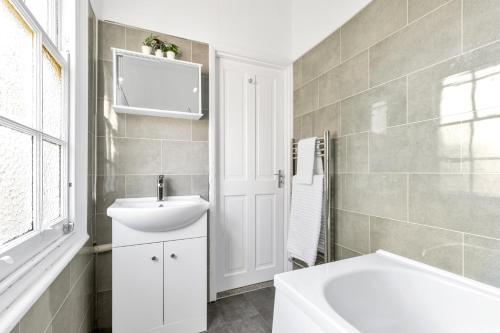 a white bathroom with a sink and a tub at Modern Two Bedroom Apartment with Free Parking! in London