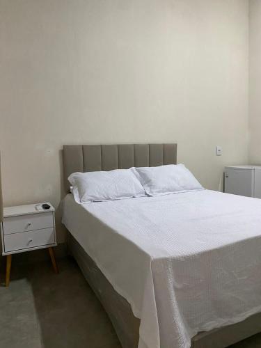 Schlafzimmer mit einem Bett mit weißer Bettwäsche und einem Nachttisch in der Unterkunft Hospedagens Express II in Chapada dos Guimarães