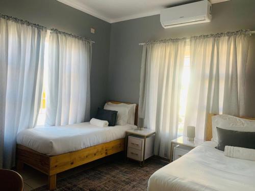 a bedroom with two beds and a window with curtains at Mmaset Houses bed and breakfast in Gaborone