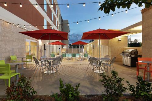 a patio with tables and chairs and red umbrellas at Home2 Suites By Hilton Savannah Airport in Savannah