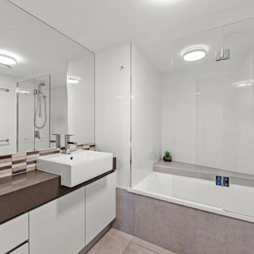 a white bathroom with a sink and a bath tub at The Mirage Resort Alexandra Headland in Alexandra Headland