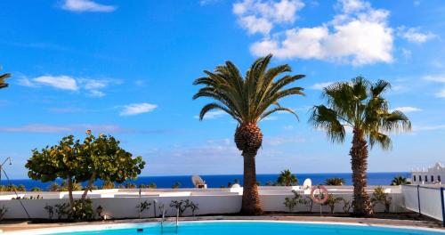 a pool with palm trees and the ocean in the background at Ocean & Pool view Puerto del Carmen in Puerto del Carmen