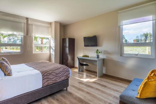 a bedroom with a bed and a desk and window at Hotel Xue Sabana in Cajicá
