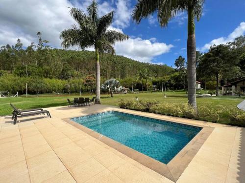 a swimming pool with a bench and palm trees at Lindo sítio para você e sua família! in Guararema