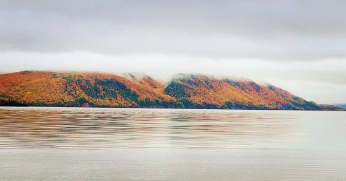 a mountain with autumn leaves on it next to a body of water at St Ann's Motel & Cottage in Baddeck
