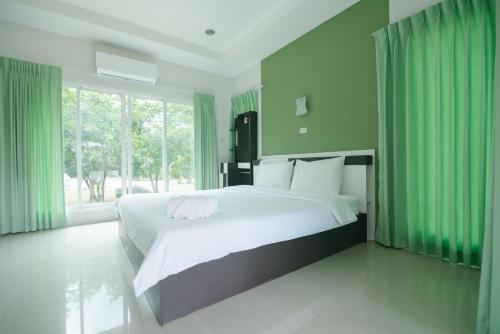 a bedroom with a large white bed with green curtains at รีสอร์ท เรือนชมดาว in Ban Nong Ban Kao