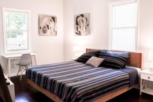 een slaapkamer met een bed met een gestreept dekbed en 2 ramen bij Eagle's Aerie Stunning 3bdrm Destination Home in Durham