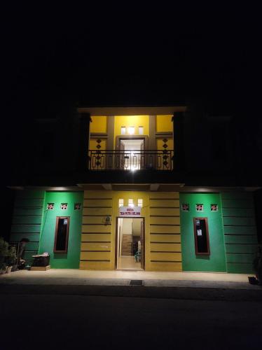 Topoyo的住宿－Wisma Tiga Putra Belawa 1，夜晚有绿色和黄色外墙的房子