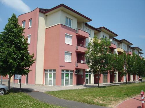 a large pink building with trees in front of it at Csabai Apartman in Bük