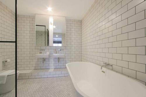 a white tiled bathroom with a tub and a sink at The Prince 228 Kingston ACT in Canberra