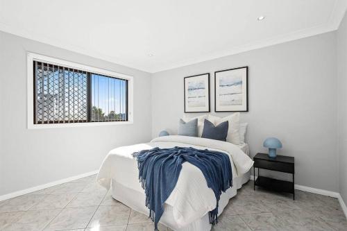 a white bedroom with a bed and a window at Ocean-View Retreat for Family Getaways in Cringila