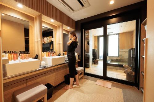 una donna in piedi di fronte a uno specchio del bagno di HOTEL Cargo Shinsaibashi ad Osaka