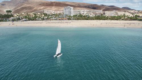 a small sail boat in the water near a beach at ROBINSON JANDIA PLAYA - Adults only in Morro del Jable