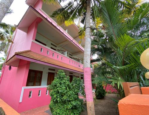 a pink building with palm trees in front of it at Packbag Comfort Bed & Breakfast in Kovalam