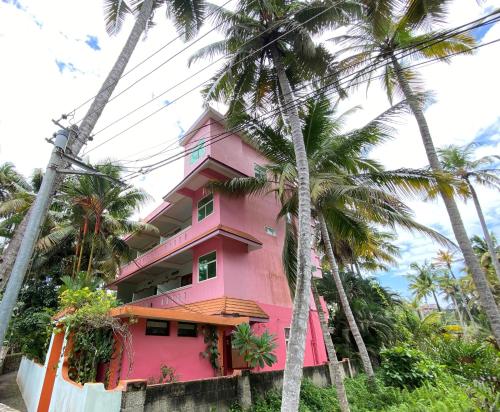 a pink house with palm trees in front of it at Packbag Comfort Bed & Breakfast in Kovalam