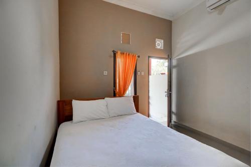 ein Schlafzimmer mit einem weißen Bett und einem orangenen Vorhang in der Unterkunft OYO Life 92838 Kost Ibu Surya in Negara