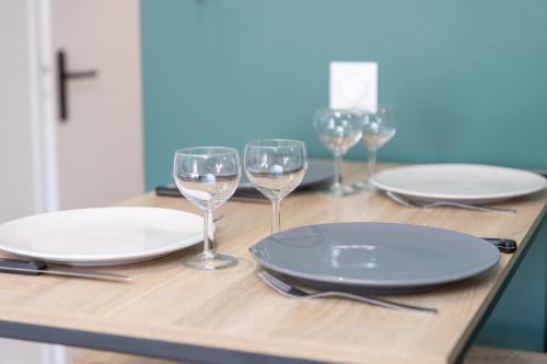 a wooden table with plates and wine glasses on it at KASA NOVA - Tout équipé & CLIMATISATION in Saint-Chamond
