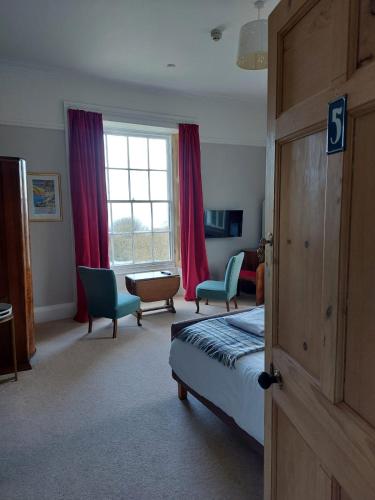 a bedroom with a bed and chairs and a window at Laston House in Ilfracombe