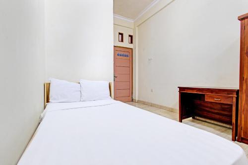 a bedroom with a white bed and a wooden desk at OYO Life 92663 Karmel 6 in Purwokerto