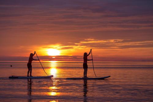 two people are standing on paddle boards in the water at sunset at Sandy Kelt - Irish House Apartments in Kalajoki
