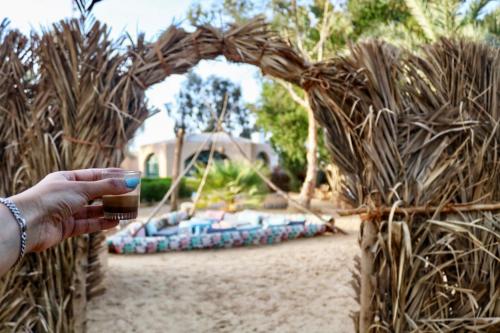 a person holding a wine glass in front of a wicker arch at Seliyaa Siwa Inn Hotel in Siwa