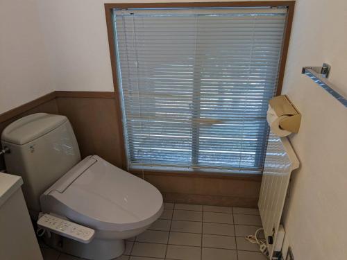 a bathroom with a toilet and a window with blinds at Shiki&Kura in Kurashiki