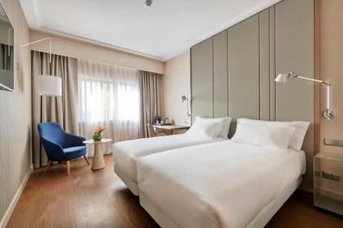 um quarto de hotel com uma grande cama branca e uma cadeira azul em NH Lisboa Campo Grande em Lisboa
