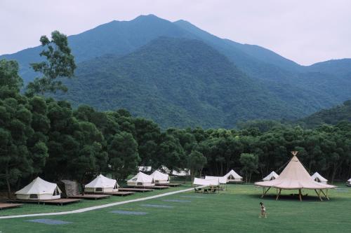 um grupo de tendas num campo com montanhas ao fundo em NatureLand Campsite em Shenzhen
