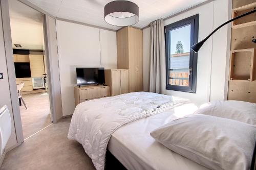 Schlafzimmer mit einem weißen Bett und einem TV in der Unterkunft Le Chalet d'Angel in Jullouville-les-Pins