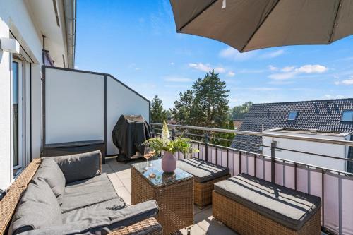 einen Balkon mit einem Sofa, Stühlen und einem Sonnenschirm in der Unterkunft SEEview Maisonette in direkter Seenähe in Friedrichshafen