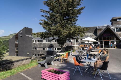 une femme assise à une table devant un bâtiment dans l'établissement Belambra Clubs Superbesse - Le Chambourguet, à Super-Besse