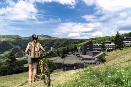 Una donna in piedi accanto a una bicicletta su una collina di Belambra Clubs Superbesse - Le Chambourguet a Super Besse