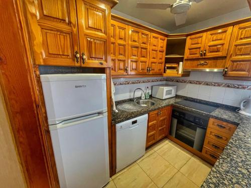 a kitchen with wooden cabinets and a white refrigerator at Puertito Varadero in Puerto de Santiago