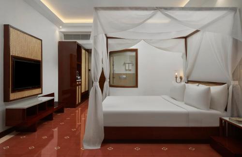 a bedroom with a white bed and a television at Radisson Blu Resort, Goa in Cavelossim