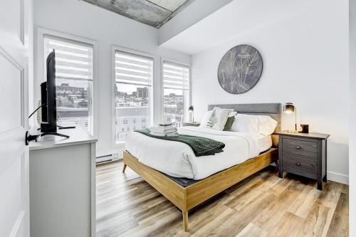 a bedroom with a bed and a tv and windows at Panorama Penthouse- piscine, gym et vue sur Québec in Quebec City