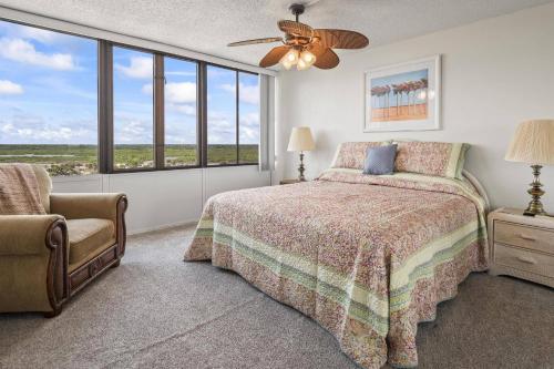 a bedroom with a bed and a chair and windows at Nautilus Sunset Escape 801 | Flagler Beach in Flagler Beach