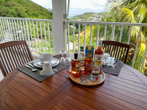 a wooden table with food and drinks on a balcony at Appartement SERENITE, tout confort 2adultes 1 enft in Les Trois-Îlets