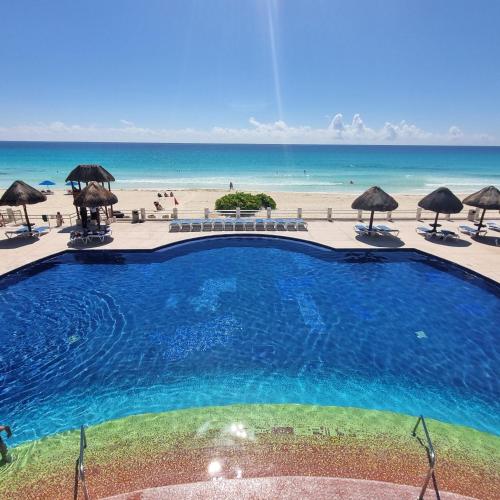 a swimming pool next to a beach with umbrellas at Villas Marlin 108, a pie de playa, albercas, jacuzi, ubicacion inmejorable in Cancún