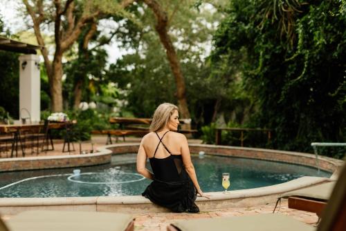 a woman in a black dress sitting next to a swimming pool at Upington African Vineyard Boutique Hotel & SPA in Kanoneiland