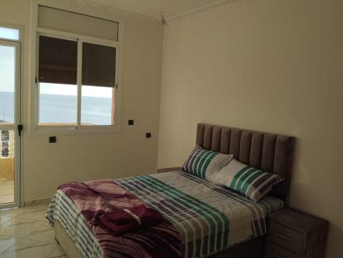 a bedroom with a bed and a window with the ocean at AlMohit Larache in Larache