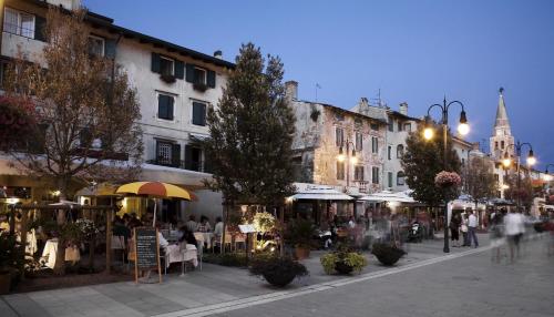 a city street with people sitting at tables and umbrellas at Albergo alla Spiaggia in Grado