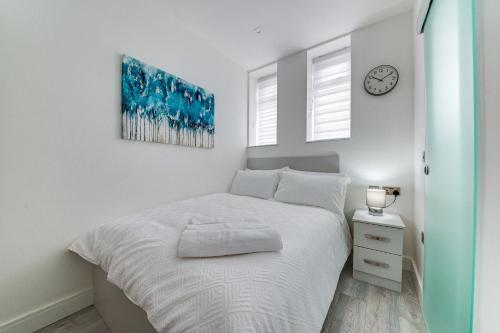 a white bedroom with a bed and a clock on the wall at Superior Compact Studio Close to Amenities in Leeds