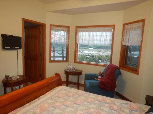 a bedroom with a bed and a chair and windows at Rocky Mountain View Bed & Breakfast in Cochrane