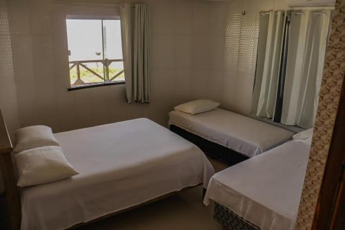 two beds in a small room with a window at Pousada Farol da Barra in Tutóia