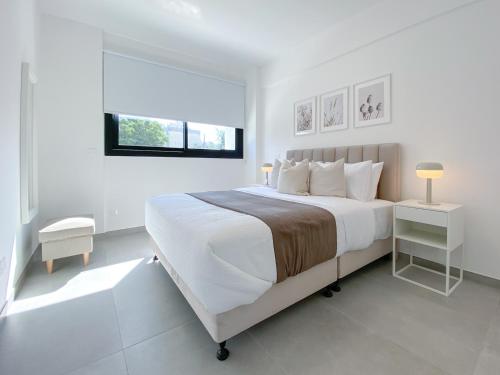 a white bedroom with a large bed and a window at Phaedrus Living White Hills Suites Panoramic View in Aglantzia