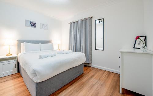 a bedroom with a large white bed and wooden floors at Bright Cosy Cottage with Parking and Outdoor Patio in London