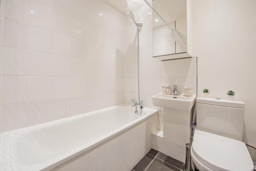 a white bathroom with a tub and a toilet at Bright Cosy Cottage with Parking and Outdoor Patio in London